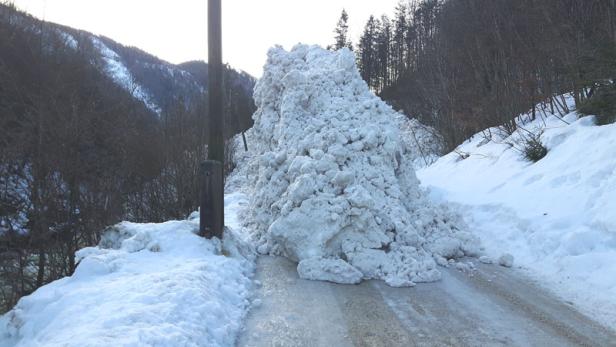 Eine Lawine blockiert eine schneebedeckte Straße in einer bergigen Landschaft.