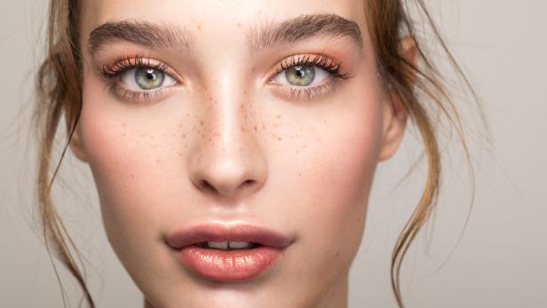 Porträt einer jungen Frau mit Sommersprossen und glänzendem Lippenstift.