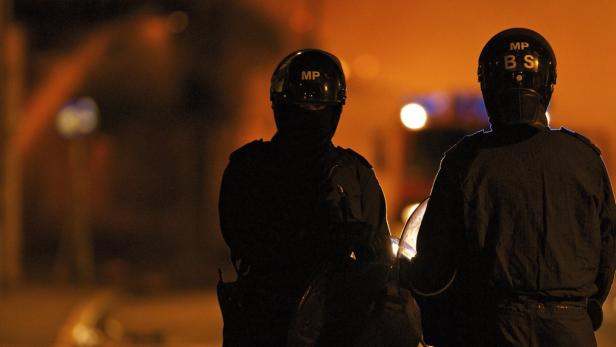Zwei Polizisten mit Helmen stehen im Dunkeln.