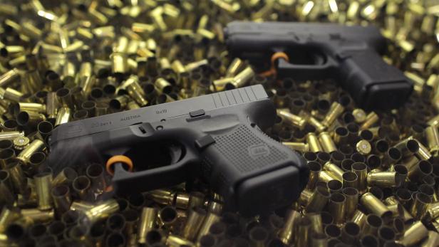 Zwei schwarze Glock-Pistolen liegen auf einem Haufen leerer Patronenhülsen.