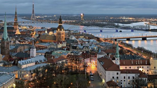 Ein Panoramablick auf die Stadt Riga mit ihren Türmen und Brücken bei Dämmerung.