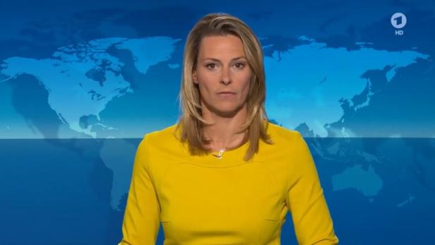 Eine Nachrichtensprecherin in einem gelben Kleid vor einer Weltkarte.