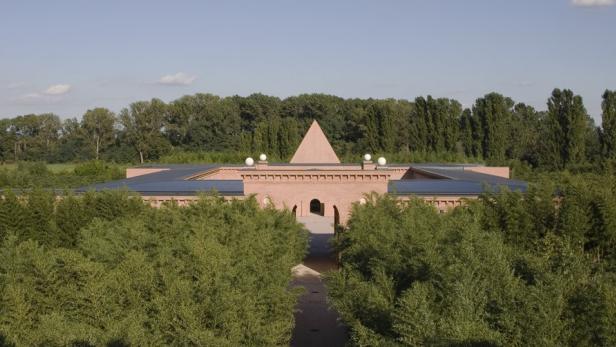 Ein Backsteingebäude mit einer Pyramide auf dem Dach, umgeben von Bäumen.