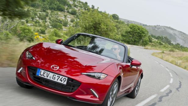 Ein roter Mazda MX-5 fährt auf einer kurvenreichen Straße.