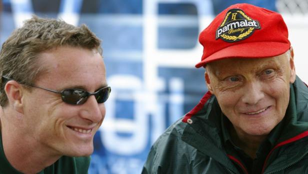 Niki Lauda mit roter Parmalat-Kappe und ein Mann mit Sonnenbrille lächeln.