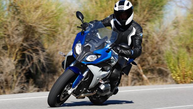 Ein Motorradfahrer fährt mit einer BMW R1200 RS auf einer Landstraße.