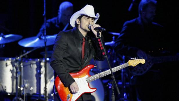 Brad Paisley tritt mit Gitarre und Cowboyhut auf einer Bühne auf.