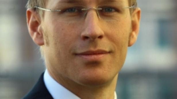 Ein Mann mit Brille, Anzug und Krawatte blickt in die Kamera.