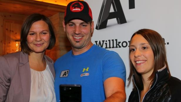 Drei Personen posieren lächelnd vor einer Wand mit dem A1-Logo.