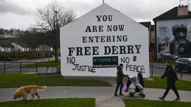People walk past a wall showing "No Justice No Peace" fresh graffiti at the Derry corner in Londonderry