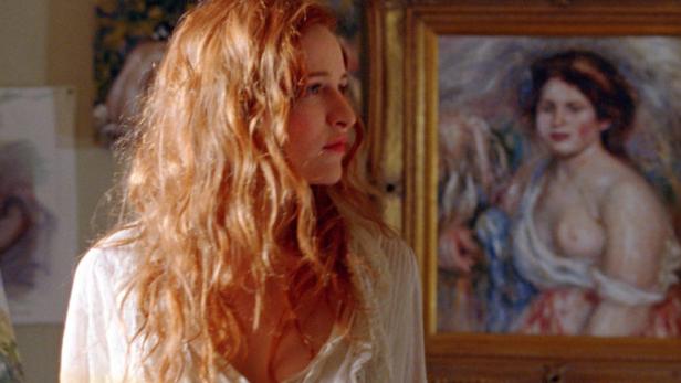 Eine Frau mit roten Haaren vor mehreren Gemälden im Stil von Renoir.