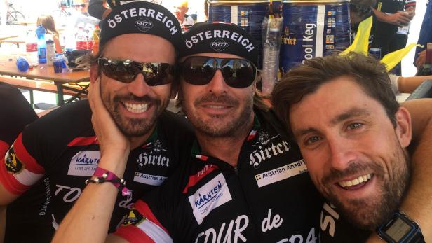 Drei Männer posieren in Radsportbekleidung mit Österreich-Bezug für ein Selfie.