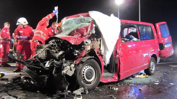 Ein schwer beschädigter roter Van nach einem Unfall, umgeben von Rettungskräften.