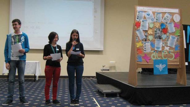 Drei Jugendliche präsentieren auf einer Bühne ein Projekt mit dem Titel „aces“.