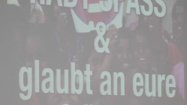 Eine Gruppe von Menschen steht hinter einem Schild mit der Aufschrift „Habt Spaß & glaubt an eure Stärken“.