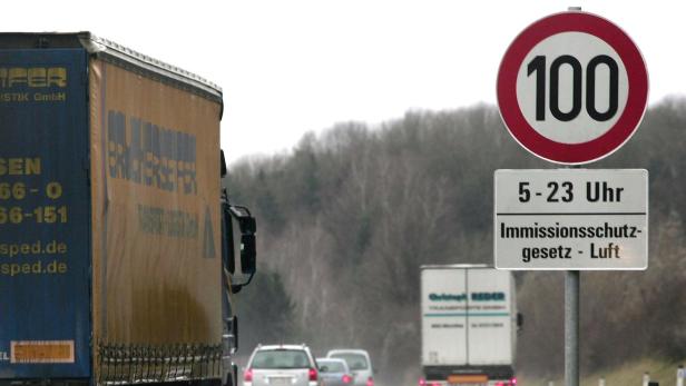Auf einer Autobahn fahren mehrere LKW und PKW; ein Schild zeigt Tempo 100 und Immissionsschutz an.