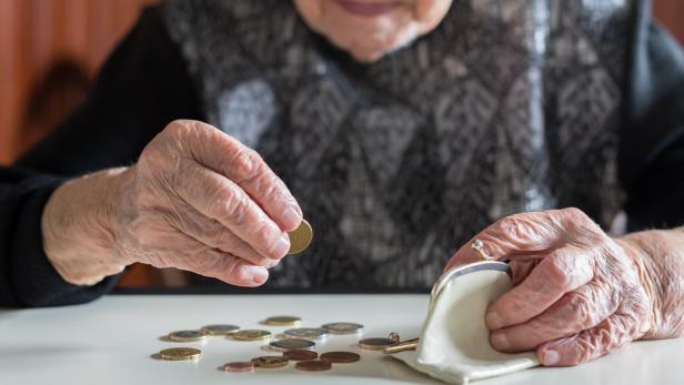 Elderly woman sitting at the table counting money in her wallet.