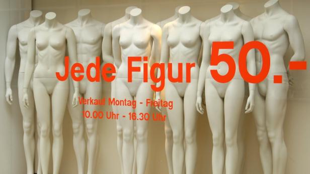 Mehrere Schaufensterpuppen stehen hinter einem Schild, das mit „Jede Figur 50,-“ wirbt.