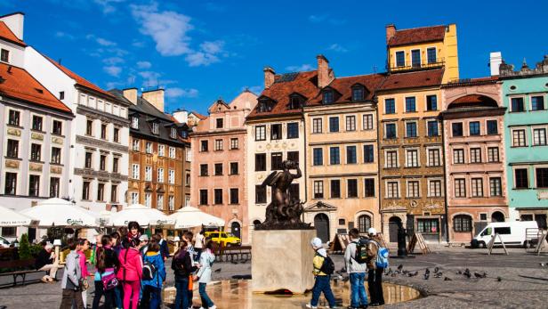 Eine Gruppe von Kindern steht auf dem Marktplatz in Warschau um einen Brunnen.