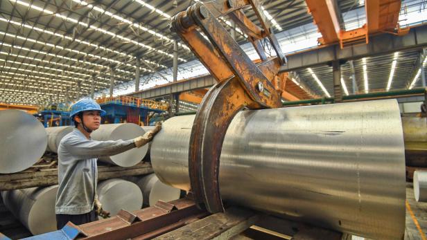 Ein Arbeiter in einer Fabrik hantiert mit einem großen Metallzylinder.