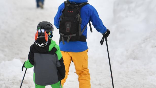 Ein Vater und sein Kind stehen mit Skiern und Stöcken im Schnee.