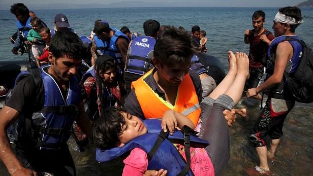 Menschen verlassen ein Schlauchboot am Ufer, einige tragen Schwimmwesten.