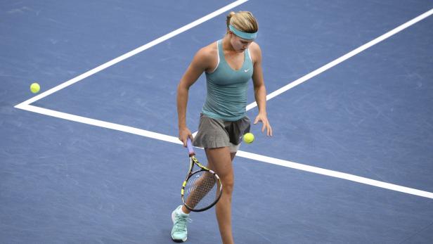 Eine Tennisspielerin auf einem blauen Platz mit gelben Bällen.