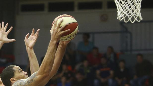 Ein Basketballspieler mit Tätowierungen wirft einen Ball in Richtung Korb.