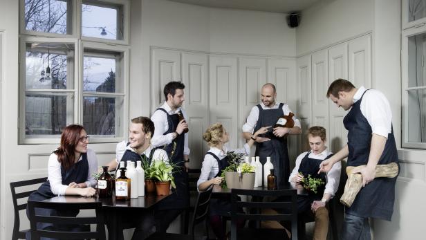 Mehrere Personen sitzen an Tischen und beschäftigen sich mit Pflanzen und Flaschen.