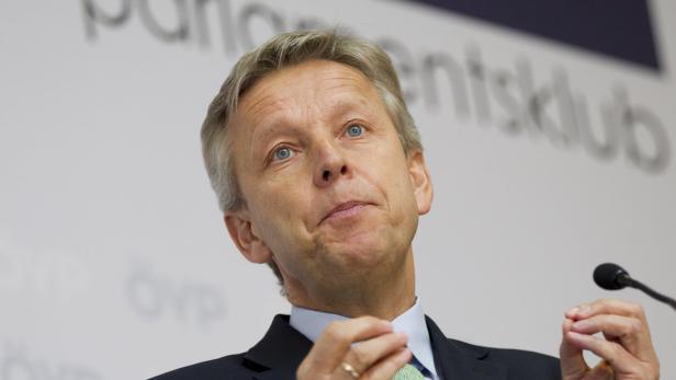 Ein Mann mit hellblauen Augen gestikuliert vor einem Mikrofon.