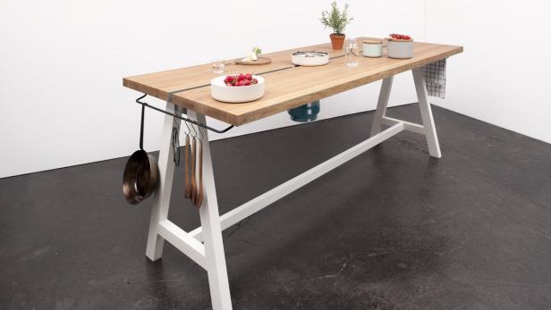 Ein Küchentisch mit Kochutensilien und Lebensmitteln steht in einem Raum.