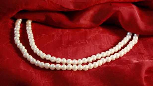 Eine zweireihige Perlenkette liegt auf einem roten Stofftuch.