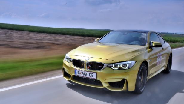 Ein goldener BMW M4 fährt auf einer Landstraße.