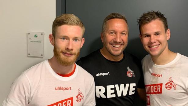 Drei Männer posieren in T-Shirts des 1. FC Köln für ein Foto.