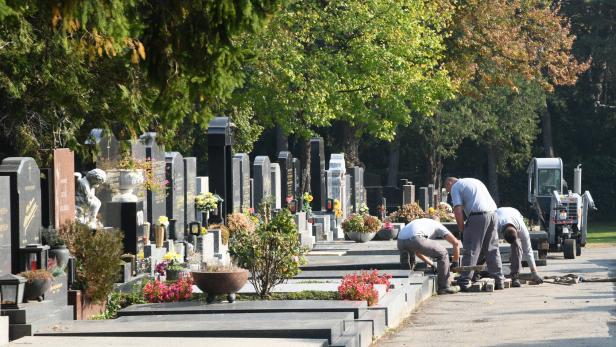 Drei Arbeiter verlegen Pflastersteine auf einem Friedhof.