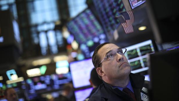 Ein Börsenhändler mit Brille blickt auf die Anzeigetafeln der Wall Street.