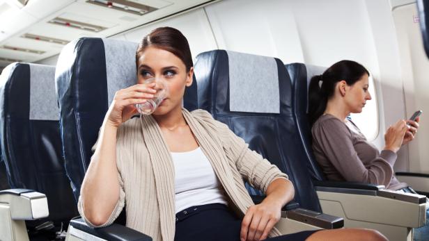 Frau im Flugzeug trinkt aus Glas