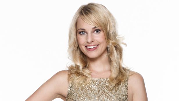 Eine lächelnde Frau mit blonden Haaren und einem goldenen Kleid vor einem weißen Hintergrund.