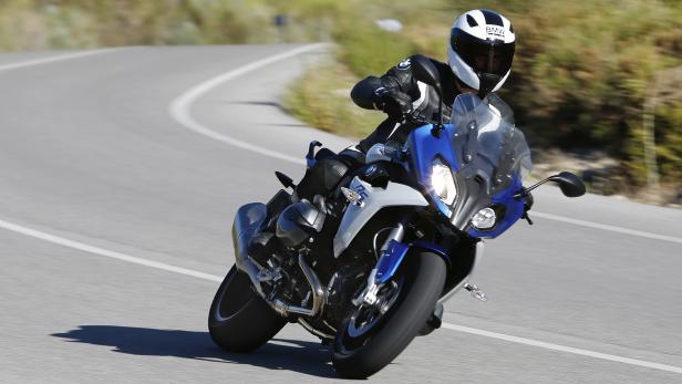 Ein Motorradfahrer fährt mit einer blauen BMW auf einer kurvenreichen Straße.