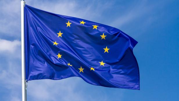 Flag of the European Union waving in the wind on flagpole against the sky with clouds
