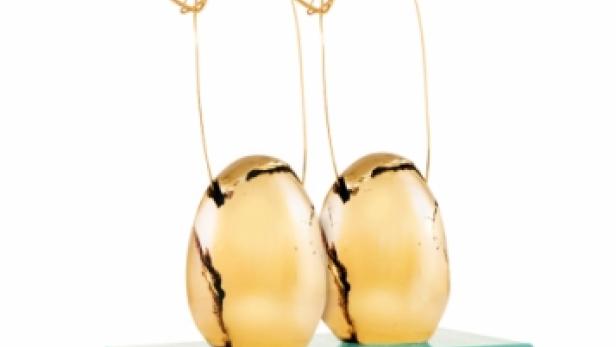 Zwei goldene Eier stehen auf einem zweistufigen, türkisfarbenen Sockel und sind mit goldenen Drahtfiguren verziert.
