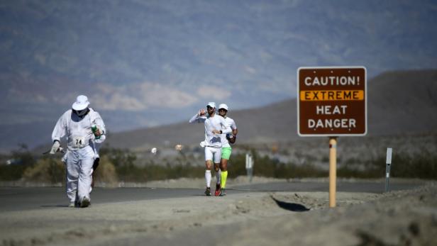 Läufer nehmen an einem Rennen im Death Valley teil, ein Warnschild weist auf extreme Hitze hin.
