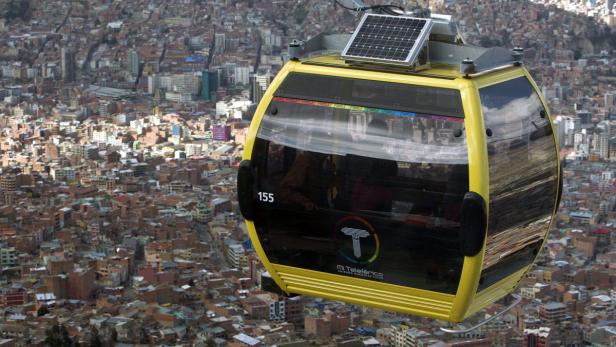 Eine gelbe Gondel der Seilbahn „Mi Teleférico“ schwebt über einer Stadt.