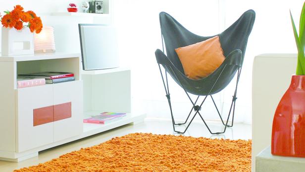 Ein Wohnzimmer mit einem Sessel, einem Teppich und einem weißen Sideboard.