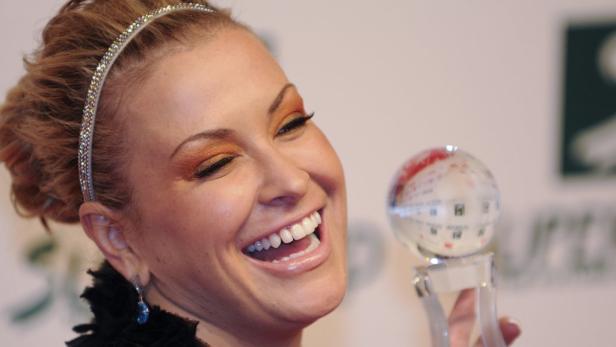 Eine Frau mit einem glitzernden Haarband lacht und hält eine gläserne Weltkugel in der Hand.