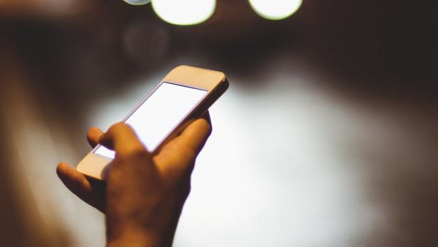 Eine Hand hält ein Smartphone mit hellem Bildschirm im Dunkeln.