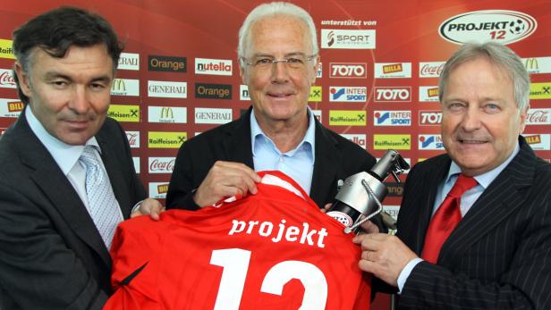 Drei Männer präsentieren ein rotes Fußballtrikot mit der Aufschrift „projekt 12“.