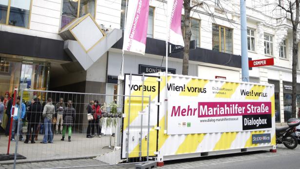 Eine Dialogbox der Stadt Wien auf der Mariahilfer Straße mit wartenden Menschen.