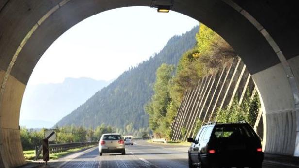 Autos fahren aus einem Tunnel in Richtung einer bewaldeten Berglandschaft.