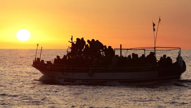 Ein Boot voller Menschen fährt bei Sonnenuntergang auf dem Meer.